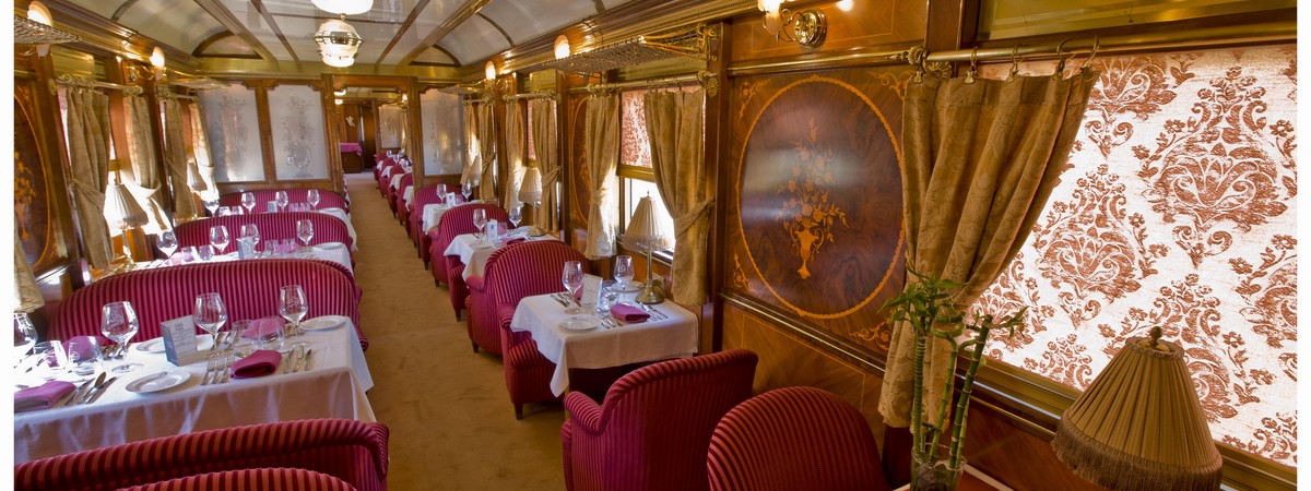 Elegant dining car interior on the Al Andalus luxury train tour; tables set with glassware and maroon seating.