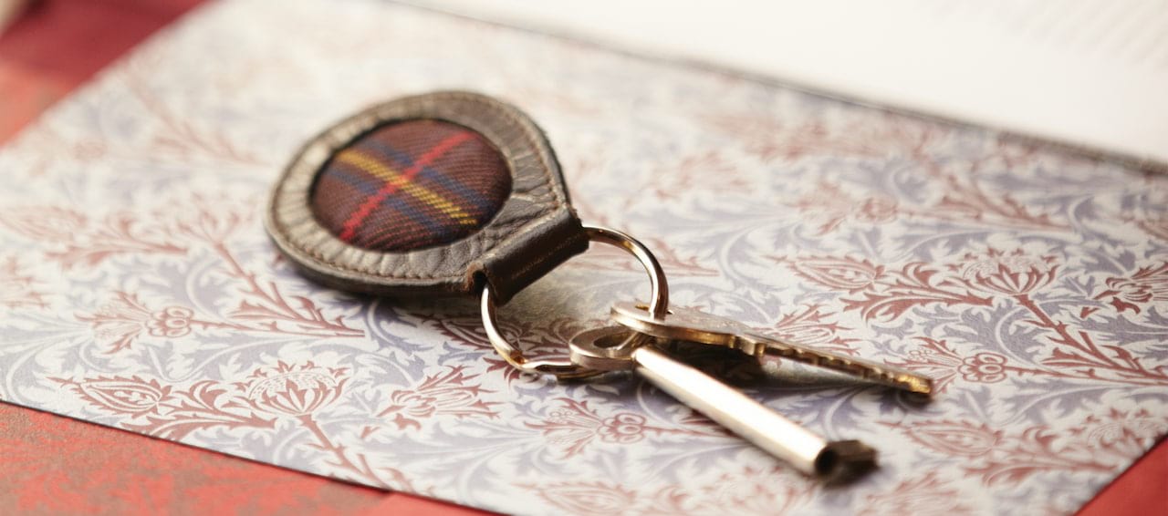 Keys with tartan fob on floral paper, suggesting access to heritage homes on the Belmond Royal Scotsman tour.