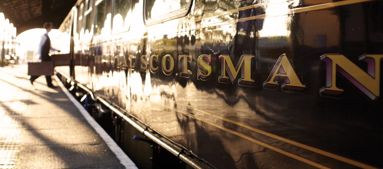 Close-up of the Belmond Royal Scotsman train with attendant boarding. Gold lettering detail on the dark carriage.