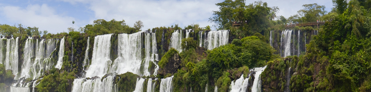 Panoramic view of Iguazu Falls, Argentina and Brazil, with lush green vegetation and walkways for viewing, part of a luxury tour.