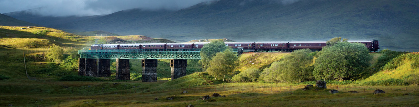The Belmond Royal Scotsman train crosses a green viaduct in the Scottish Highlands during the Western Scenic Wonders tour.